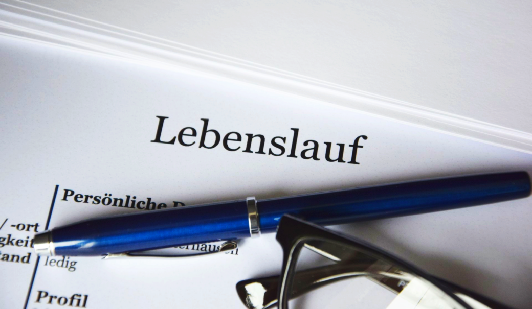 ein wei&szlig;es Blatt Papier mit dem Aufdruck Lebenslauf, daneben liegend ein Kugelschreiber und eine Brille